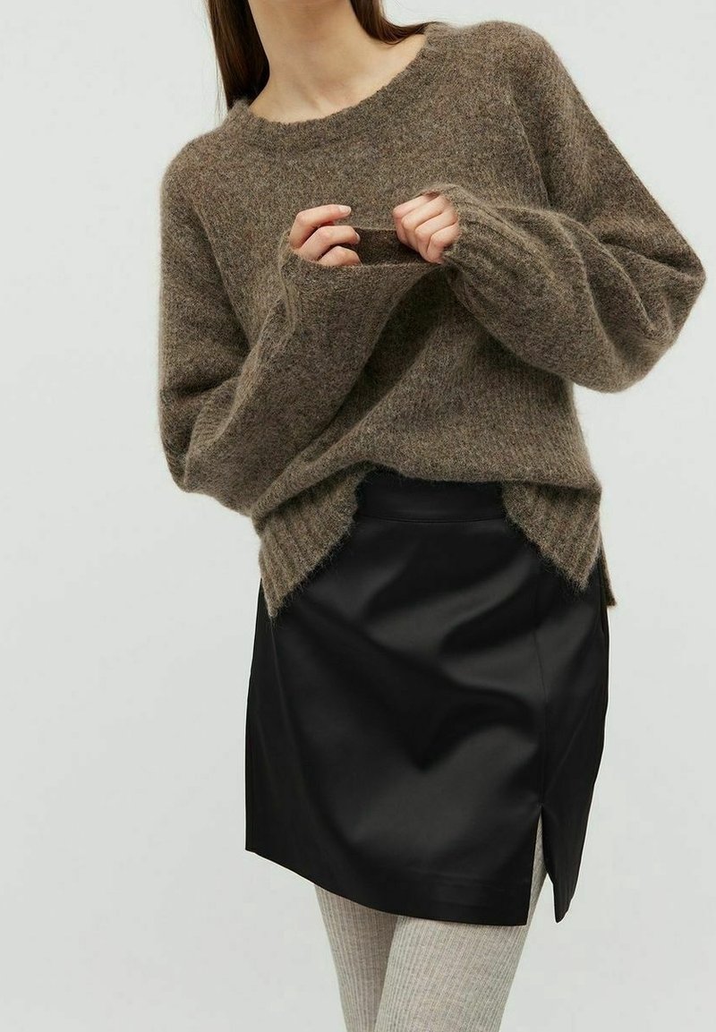Pull en laine bouclée marron avec une coupe ample, doté d'un col et de poignets côtelés, associé à une mini-jupe en cuir noir avec une fente latérale.