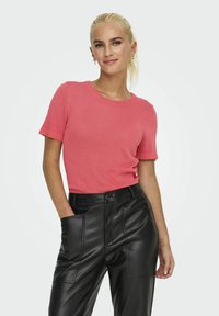 Top de punto coral de manga corta con cuello redondo, combinado con pantalones de cuero negros que tienen bolsillos delanteros y un ajuste relajado.