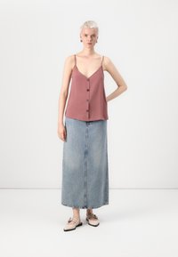 Frambozenroze camisole met een V-hals en knopen aan de voorkant, gecombineerd met een lichtblauwe denim maxi rok. Contrastaccenten in schoenen.