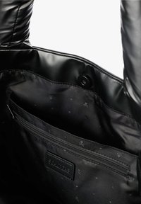 Interior de un bolso de cuero negro con forro de tela, bolsillo interno con cremallera y cierre de botón magnético, presentando un sutil patrón de calaveras y tibias cruzadas.