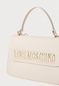 Mala de mão em imitação de couro bege com um formato estruturado, apresentando um logotipo "LOVE MOSCHINO" em tom dourado e uma pega superior para transporte.