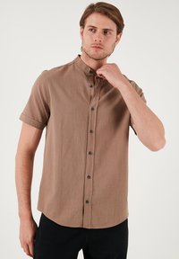 Korte mouwen overhemd met knopen van lichtbruine stof met een gestructureerde afwerking, voorzien van een mandarin collar en donkere knopen.