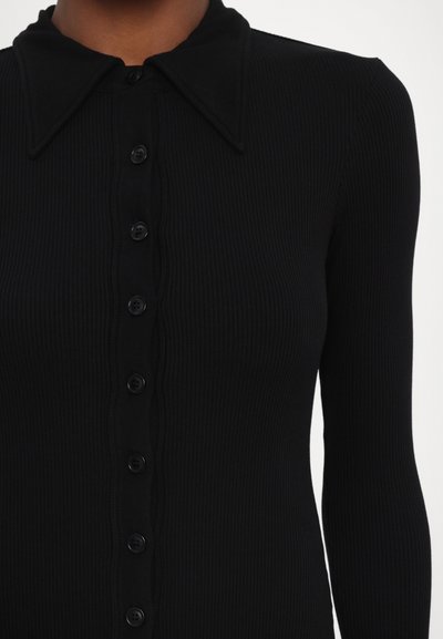 Melna ribota adīta kleita ar garām piedurknēm un strukturētu apkakli. Tai ir pogu aizdare priekšpusē ar melnām pogām.