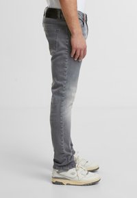 Jeans de mezclilla gris con un corte slim, con un ligero desgaste, diseño de cinco bolsillos y una cinturilla negra. Combinados con zapatillas blancas y grises.