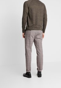 Chemise grise à manches longues avec une finition texturée, associée à un pantalon à carreaux beige et des bottines noires. Présente un ourlet incurvé et des poches.