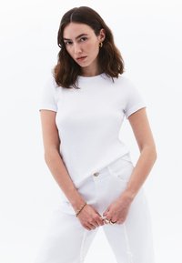 T-shirt bianco in cotone con maniche corte e scollo rotondo, abbinato a pantaloni in denim bianchi. Design semplice, texture liscia e forma aderente.