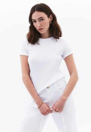 Camiseta de algodón blanca de manga corta con cuello redondo, combinada con pantalones de mezclilla blancos. Diseño simple, textura suave y forma ajustada.