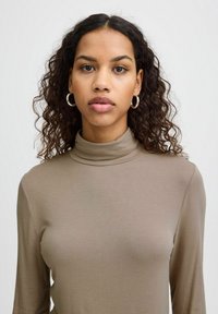 Camiseta de cuello alto ajustada de manga larga en suave tela taupe. Textura lisa con costuras mínimas y un ligero brillo. Sin patrones ni acentos visibles.