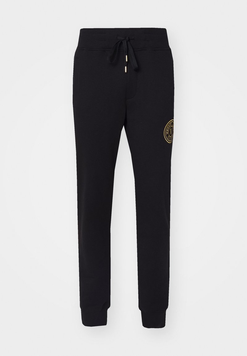 Pantalones sudadera negros en mezcla de algodón con cintura elástica y cordón, pernera ajustada, bolsillos laterales y un detalle de logo bordado en dorado en el muslo.