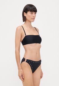 Ensemble de bikini noir comprenant un haut bandeau avec des fines bretelles et un bas orné d'accents en clous argentés et d'un détail en métal circulaire.