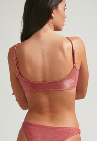 Un top de bikini metálico rosa con tirantes ajustables y una textura suave, que cuenta con un corte simple y elegante. La vista trasera muestra líneas limpias.