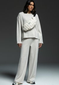 Light grey, oversized long-sleeve top with wide-leg pants and a puffy white crossbody bag, featuring a black strap and zipper.