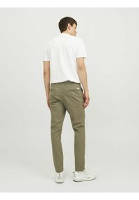 Olijfgroene chinos met een slim fit, voorzien van achterzakken en een klein wit logo-label. Gepaard met een effen witte shirt met korte mouwen.