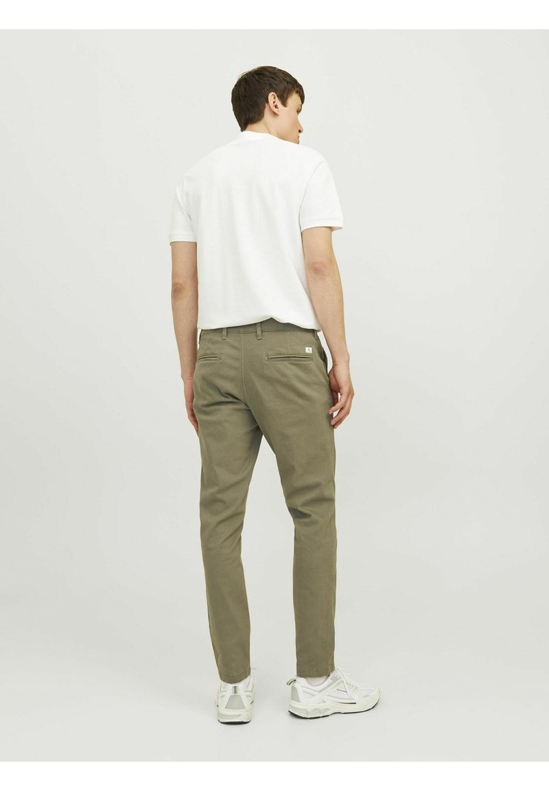 Chinos verde oliva de corte ajustado, con bolsillos traseros y una pequeña etiqueta de logo blanca. Combinados con una camisa blanca de manga corta lisa.
