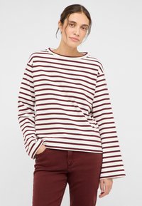 Gestreiftes langärmeliges Oberteil mit Bootsausschnitt, mit weißen und dunkelroten Streifen; weicher Baumwollstoff; lockere Passform, kombiniert mit dunkelroter Hose.