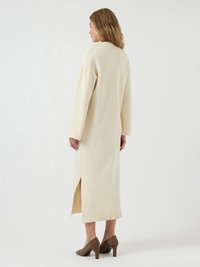 Lungo vestito avorio con una vestibilità morbida, dotato di maniche lunghe e uno spacco laterale. Tessuto dalla consistenza soffice, abbinato a scarpe con tacco marroni.