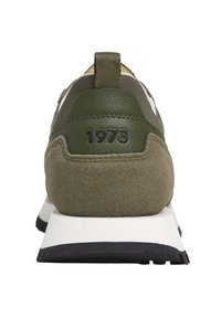 Tenisi verde măsliniu, cu un amestec de piele netedă și suede texturat, având o talpă intermediară albă și o talpă exterioară din cauciuc negru. Pe spate este inscripționat '1973'.