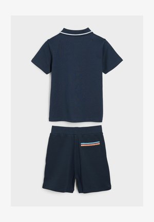 Polo de algodón azul marino con ribetes blancos, combinado con pantalones cortos azul marino que presentan un detalle de franjas multicolor en el bolsillo. Diseño casual.