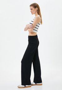 Zwarte wijde broek van een gestructureerde stof, gecombineerd met een aansluitende witte crop top met zwarte horizontale strepen. Casual witte sneakers.
