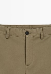 Khakihosen mit strukturiertem Gewebe, ausgestattet mit einem schwarzen Knopfverschluss, Gürtelschlaufen und einem glatten Taillenbund, die ein sauberes Design präsentieren.