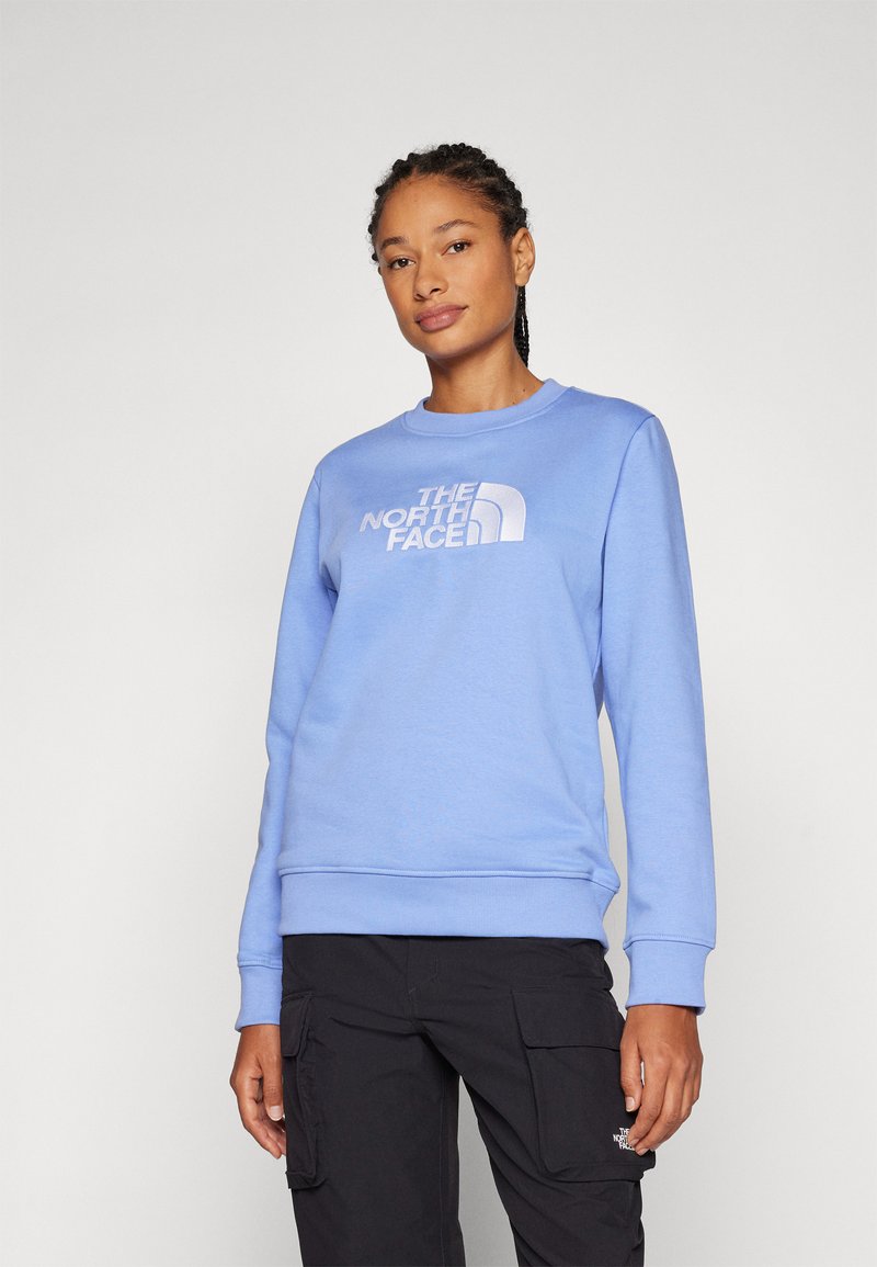 Lyseblå genser med rund hals og ribbede mansjetter. Har "The North Face"-logoen i kontrasterende hvitt tydelig vist på forsiden.