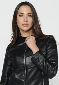 Veste en cuir noire au design ajusté, avec des détails de couture horizontale et une fermeture éclair. Texture lisse, col haut et manches longues.