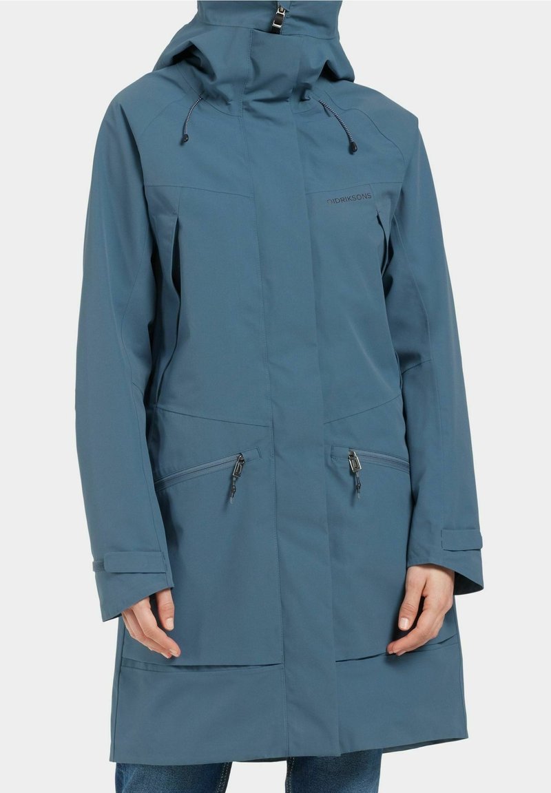 Vattentät blå ytterjacka med hög krage, justerbar huva, dragkedjefickor och slät textur. Långa ärmar med manschetter.