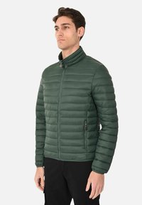 Giacca imbottita verde con colletto rialzato, chiusura frontale con zip e tasche laterali con zip; presenta una texture trapuntata orizzontale.