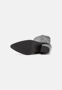 Botín negro de cuero con puntera afilada y suela de goma texturizada. Presenta un upper liso con costuras mínimas y un tacón bajo.