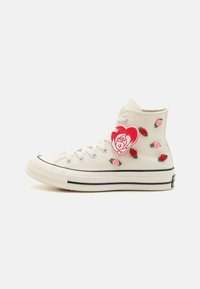 Høye sneakers i kanvas i kremfarge, med rosebroderi i rødt og rosa, gummitåhette, svart striping og hjerteformet merkesymbol.