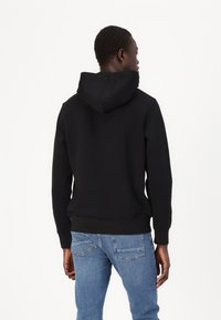 Sorte hættetrøje med kængurulomme, tekstureret stof, ribbede manchetter og kant, vist fra ryggen med blå denim jeans.