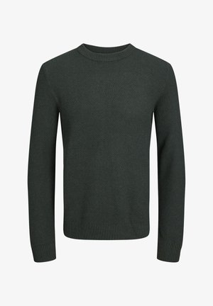 Dziecko w ciemnozielonym swetrze o fakturze, czarnych spodniach cargo z bocznymi kieszeniami i czarnych trampkach z białymi podeszwami, stojące na jednolitym tle.