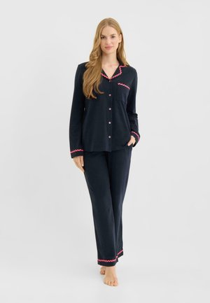 Marineblåt pyjamasæt i blødt stof med en knaplukket top med lyserød bølget kant og matchende bukser med bølget kantdetalje.