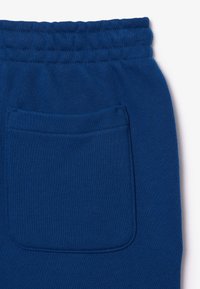 Blauwe sweatpants van een zachte, textuurrijke stof, met een elastische tailleband en een enkele achterzak met stikseldetails.