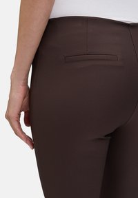 Brązowe legginsy o gładkiej fakturze; posiadają małą kieszonkę z tyłu i są dopasowane, podkreślając dopasowany krój.
