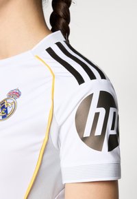 Biela športová dres s čiernymi a žltými pruhmi, erbom a veľkým šedým kruhovým logom s nápisom "hp". Textúrované panely na rukávoch.