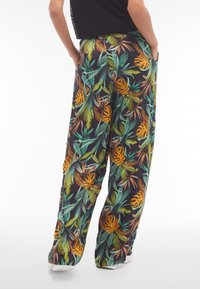 Pantalones de pierna ancha con estampado floral en negro, con hojas tropicales en verde y naranja, confeccionados en tela ligera y con bolsillos laterales.