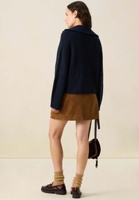 Pull en tricot militaire à côtes avec un large col, jupe en suede marron, chaussettes en tricot marron clair et chaussures sombres, agrémenté d'un petit sac.