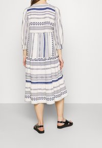 Tryckt klänning med trekvartslånga ärmar, med blå och vita geometriska mönster, lagerkjol och en lös passform. Matchad med svarta sandaler.