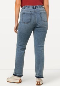 Jeans de mezclilla de color azul claro con corte relajado, cinturilla elástica y dos bolsillos traseros. El dobladillo presenta un contraste de mezclilla oscura.
