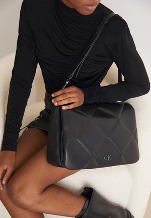 Zwarte gewatteerde leren handtas met een zilveren kettingriem en een gegraveerd logo. De tas heeft een geometrisch patroon en een gestructureerde vorm.