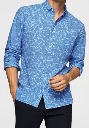 Camicia azzurro chiaro con un piccolo motivo floreale bianco, maniche lunghe arrotolate fino ai gomiti e una tasca sul petto. Tessuto di cotone liscio.