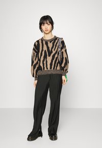 Pulôver de malha com padrão de zebra em castanho e preto; combinado com calças pretas pregueadas e sapatos pretos robustos. Apresenta uma alça com a marca.