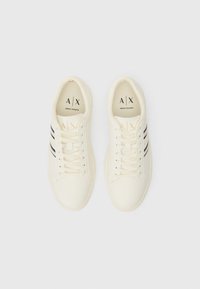 White sneakers with black stripes, smooth leather texture, round toe, and flat laces. Logo "A|X" printed inside the shoes.