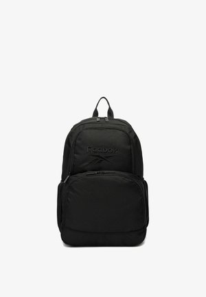 Mochila negra Reebok con asa superior, dos compartimentos con cremallera y bolsillos laterales de malla, mostrada sobre un fondo blanco.