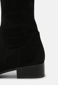 Black suede mid-calf boot with a smooth texture, rounded toe, and a low, stacked heel. Features minimal stitching and design accents.