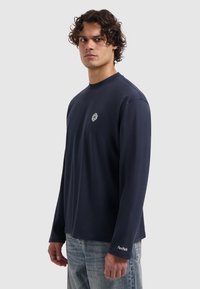 Marineblauwe longsleeve shirt van gladde stof, met een ronde hals, een klein geborduurd logo op de borst en een merknaam op de manchette.