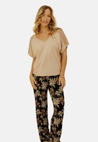 Haut beige clair en V avec des épaules à motifs, associé à un pantalon noir arborant un motif floral dans des tons dorés et bruns.
