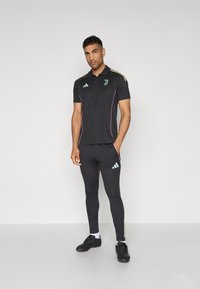Black athletic polo with short sleeves and pink accents, paired with black leggings. Features turquoise logo and three white stripes on pants.