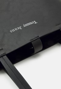 Sac fourre-tout en cuir noir avec double bandoulière et logo "Tommy Jeans" embossé en argent sur le devant supérieur.